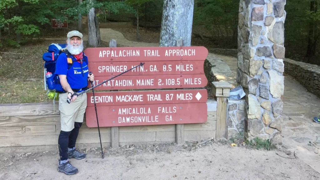 Old man hiker posing next to stone archway